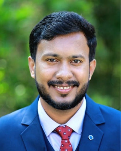Man wearing a blue suit with a red tie against a blurred green background
